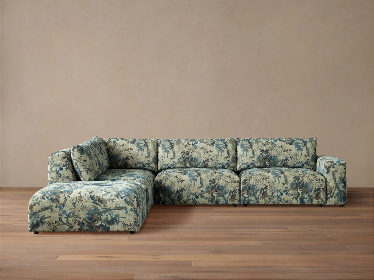 Keegan Five-Piece Sectional in L-shape, upholstered in blue, green, and brown leafy pattern, against a beige wall on a wood floor.