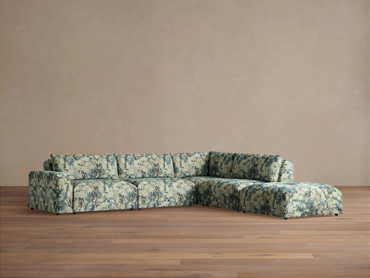 Blue and beige botanical pattern Keegan Five-Piece Sectional with solid throw pillows, arranged in a sunlit living room.