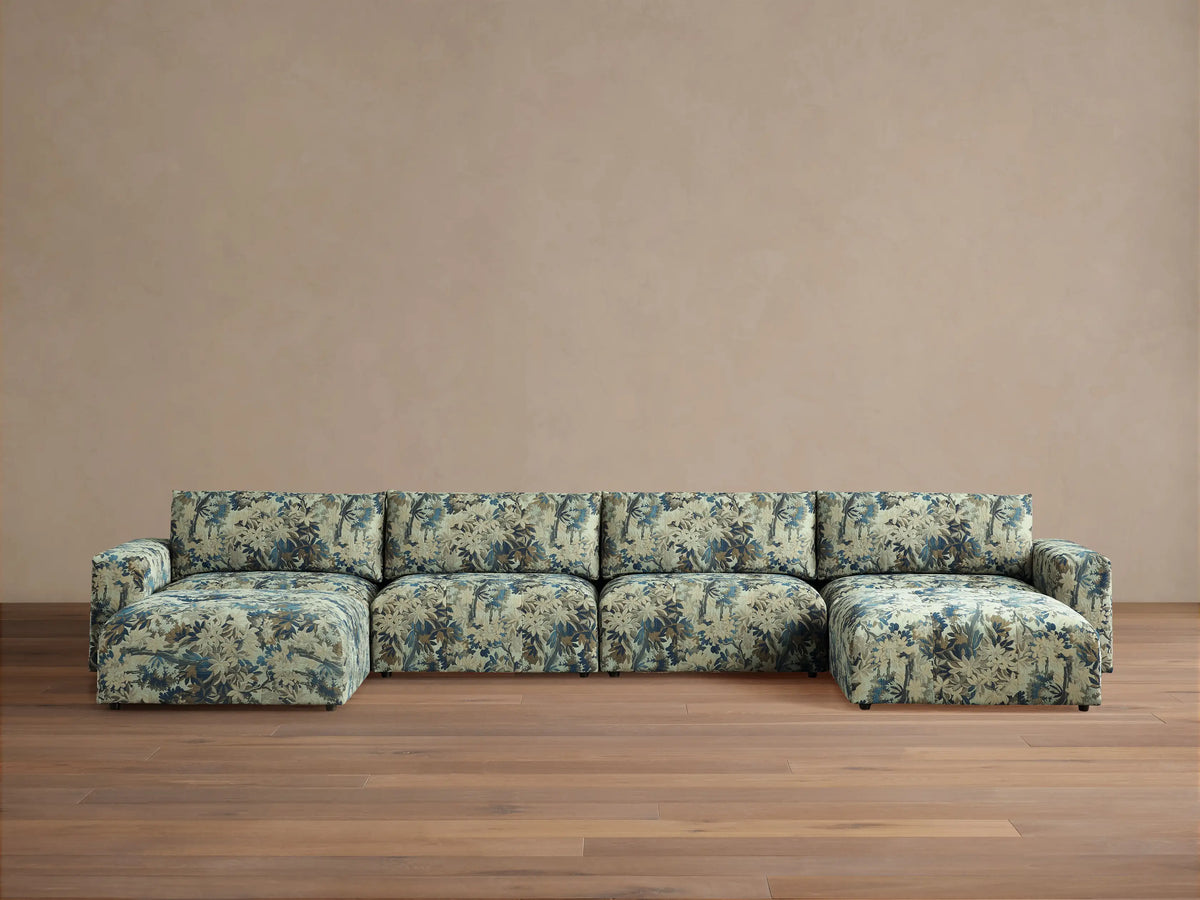 Keegan Six-Piece Sectional in light green fabric with blue tropical leaf pattern, U-shaped, on wood floor against tan wall.