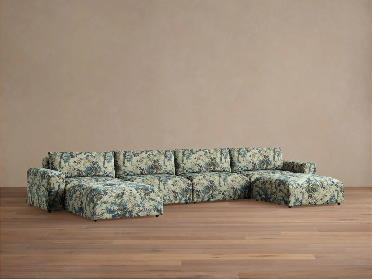 Keegan Six-Piece Sectional in light green fabric with blue tropical leaf pattern, U-shaped, on wood floor against tan wall.