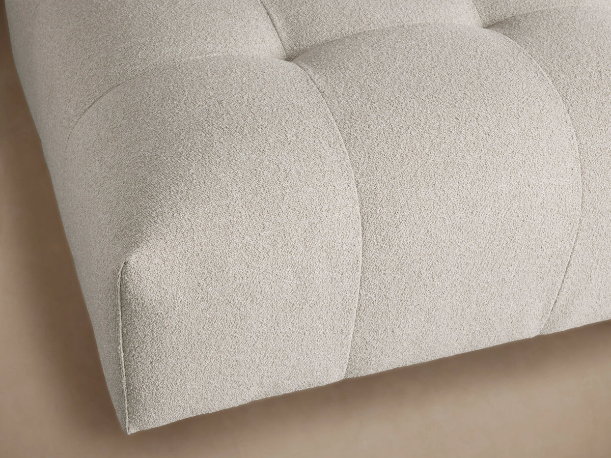 Keegan Ottoman, light gray textured fabric, low rectangular, tufted top, channel-stitched sides, on a wood floor.