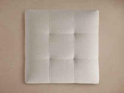 Close-up of a light beige, textured, tufted Keegan Ottoman, showing soft corners and woven fabric details from above.