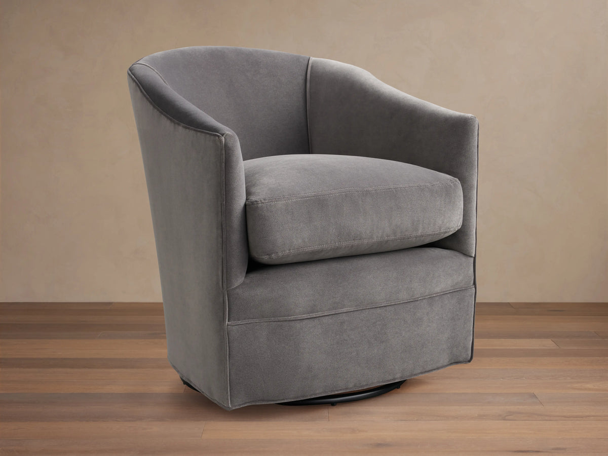 Giles Swivel Chair in dark gray fabric, featuring a curved backrest and wide seat cushion on a round base for 360-degree rotation.