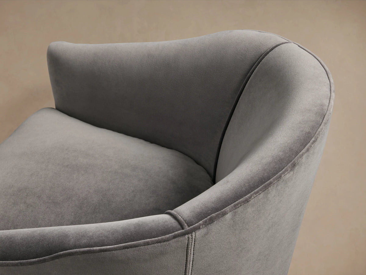 Giles Swivel Chair in gray fabric with curved backrest and plush seat cushion, on a wooden floor against a beige wall.