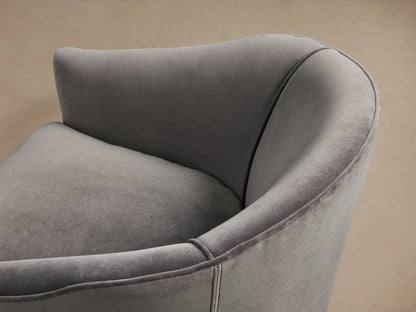 Giles Swivel Chair in gray fabric with curved backrest and plush seat cushion, on a wooden floor against a beige wall.