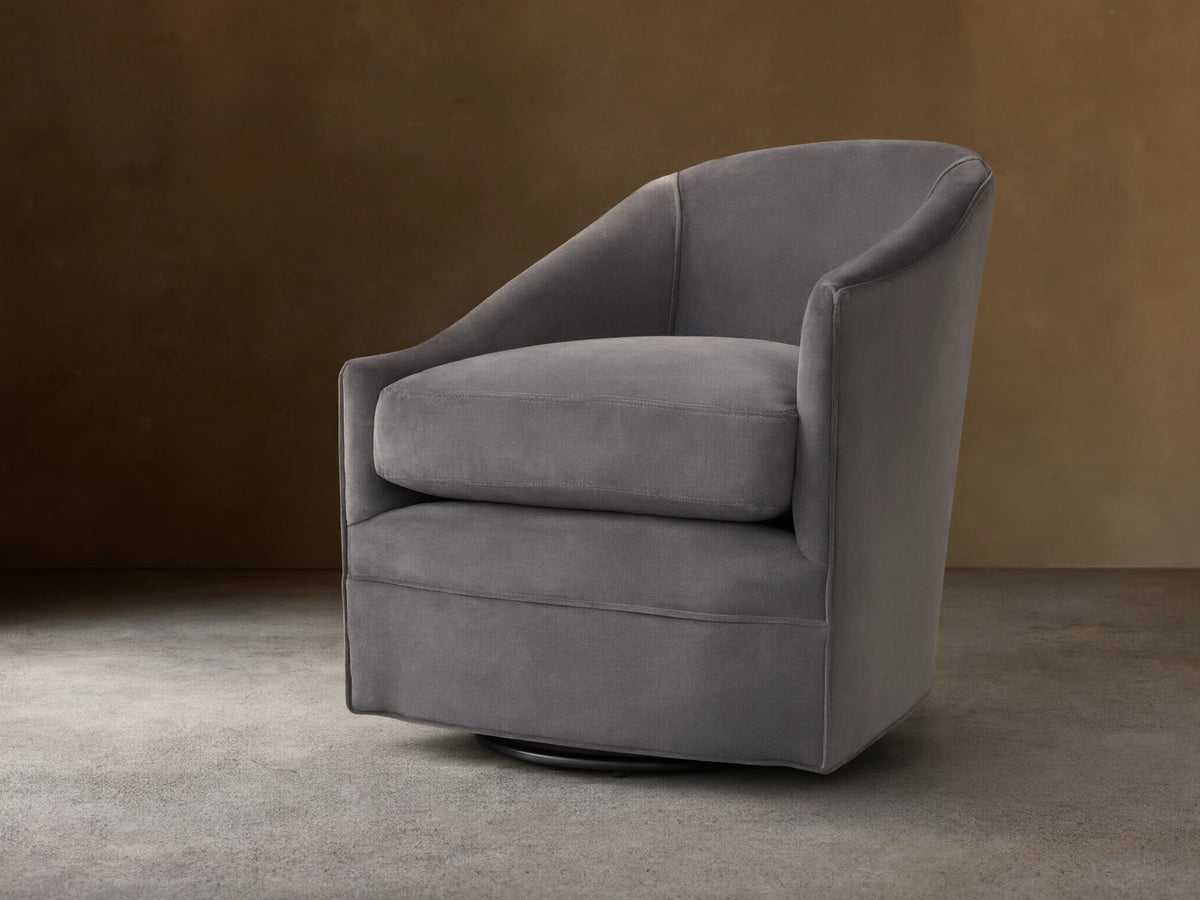 Giles Swivel Chair in dark gray fabric, featuring a curved backrest and wide seat cushion on a round base for 360-degree rotation.