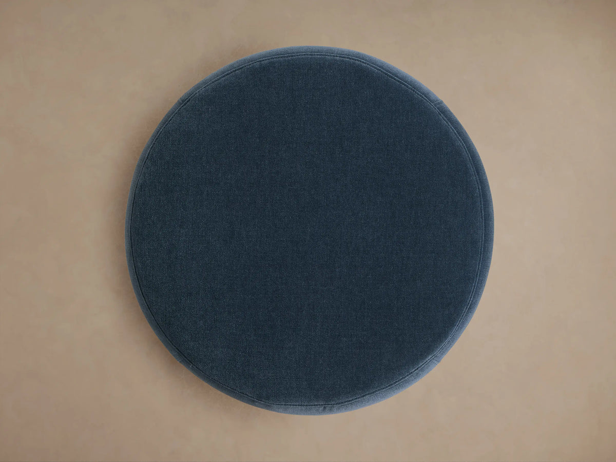 Overhead view of a circular Ryles Plinth Ottoman, upholstered in deep blue fabric, centered on a light brown floor.