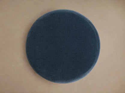 Overhead view of a circular Ryles Plinth Ottoman, upholstered in deep blue fabric, centered on a light brown floor.