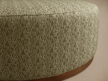 Close-up of a round Ryles Plinth Ottoman, upholstered in textured olive green and light beige flecked fabric, with a natural wood base.