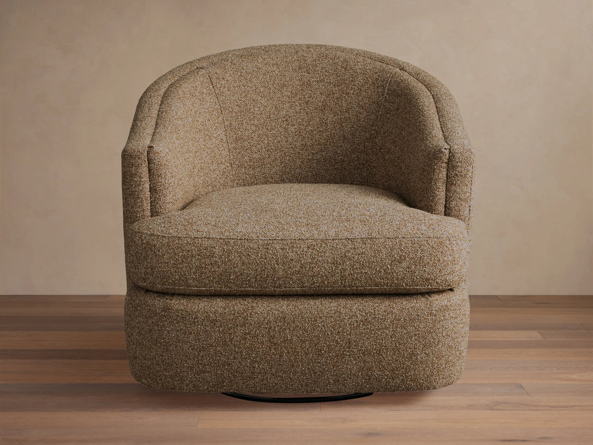 Kieran Swivel Chair with a curved backrest and cushioned seat in a textured beige fabric, placed on a wooden floor.