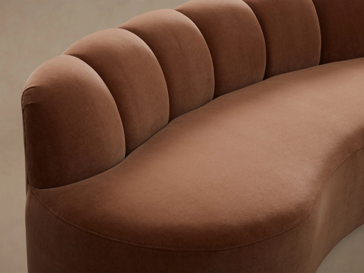 Close-up of a brown Amira Three-Piece Curved Sectional, showing its curved seat and channel-tufted backrest in velvet.