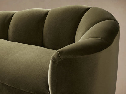 Close-up of Amira Daybed in dark olive green velvet, showing curved right arm and fluted back cushions against a soft brown wall.