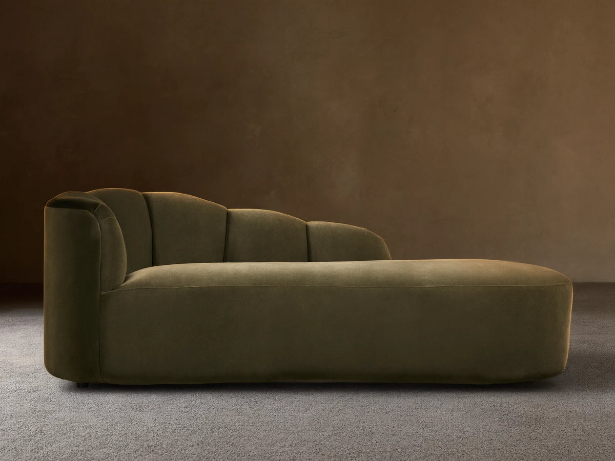 Amira Daybed: olive green velvet chaise lounge with a low, sculpturally curved backrest, on a wooden floor.