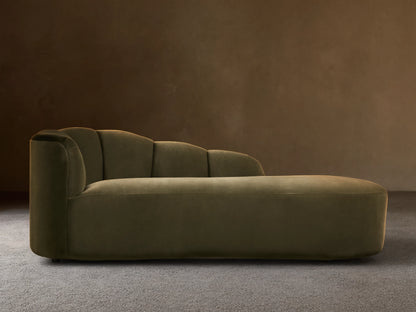 Amira Daybed: olive green velvet chaise lounge with a low, sculpturally curved backrest, on a wooden floor.
