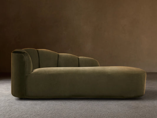 Amira Daybed: olive green velvet chaise lounge with a low, sculpturally curved backrest, on a wooden floor.