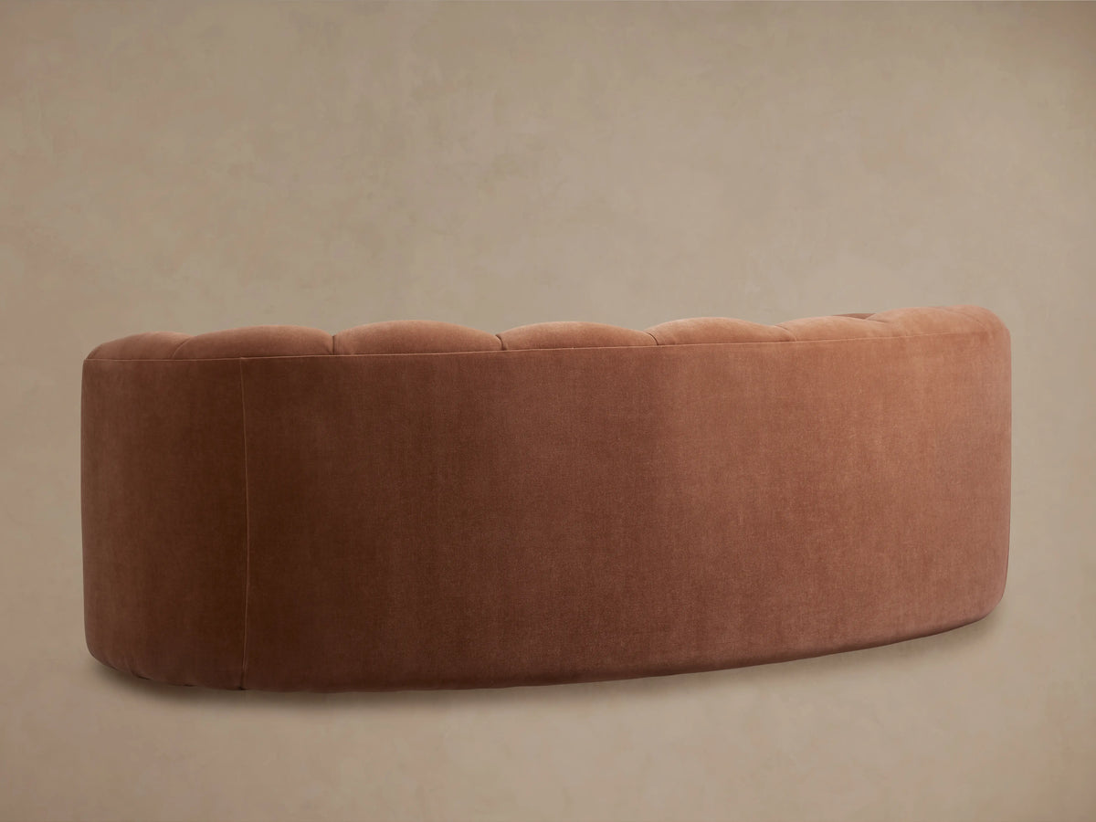 Warm brown Amira Sofa with fluted, curved back and integrated arms, on a wooden floor against a neutral wall.