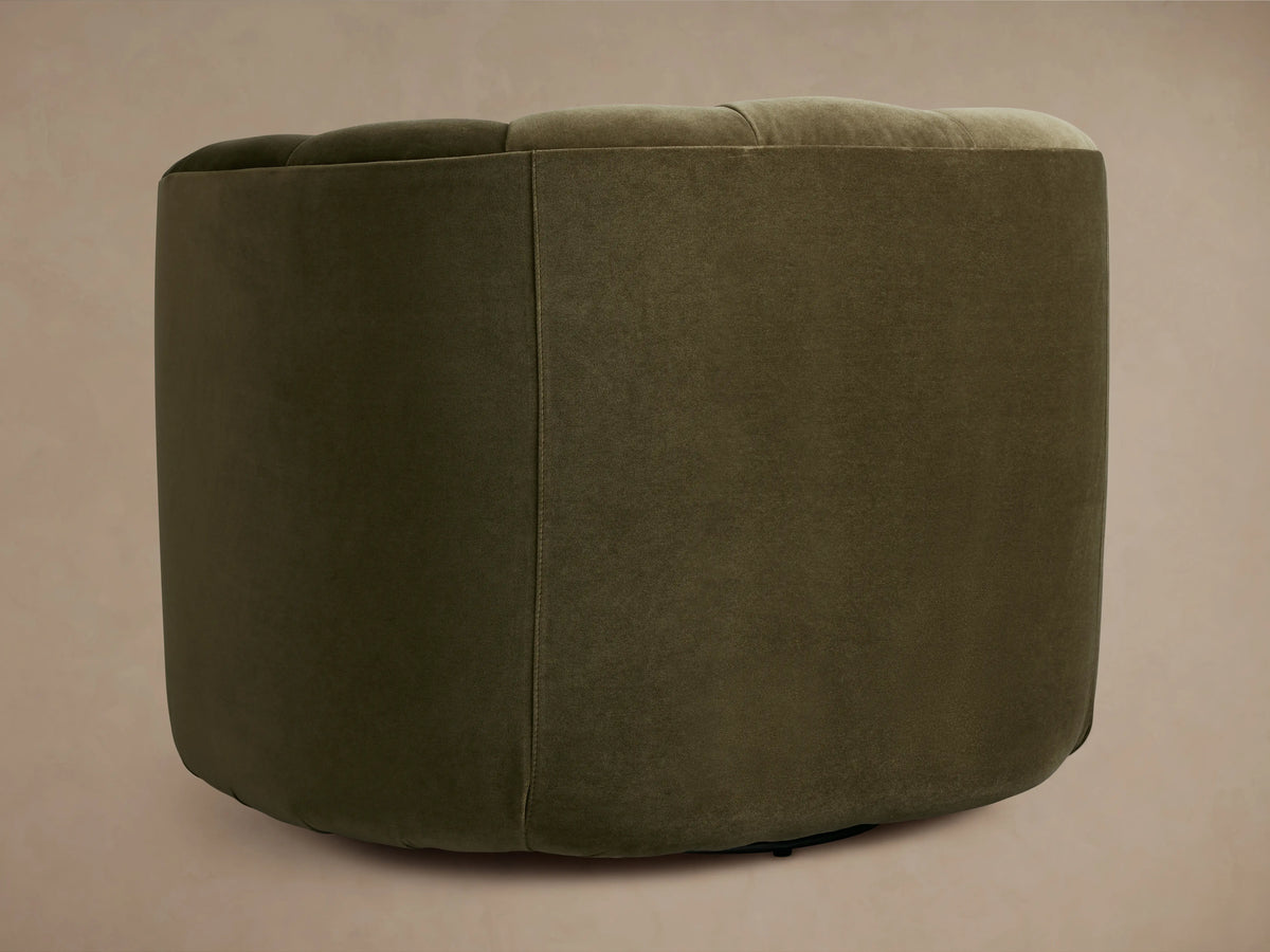 Front view of Amira Swivel Chair, dark olive green velvet with channel tufted curved back, on wood floor.
