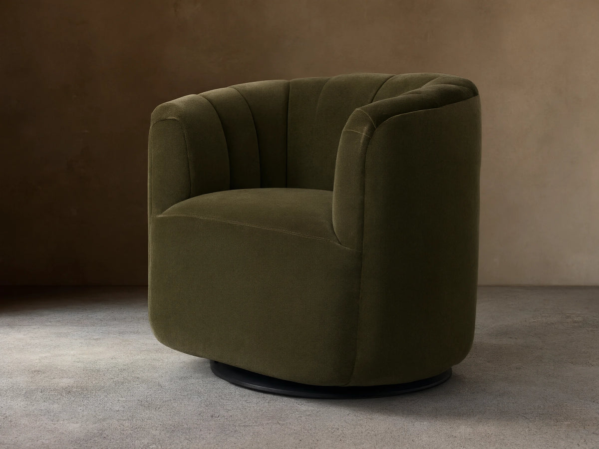 Dark olive green velvet Amira Swivel Chair, rounded form, vertical channel tufting on back, angled view on wood floor.