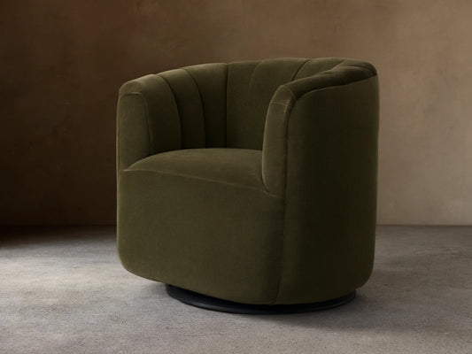 Dark olive green velvet Amira Swivel Chair, rounded form, vertical channel tufting on back, angled view on wood floor.