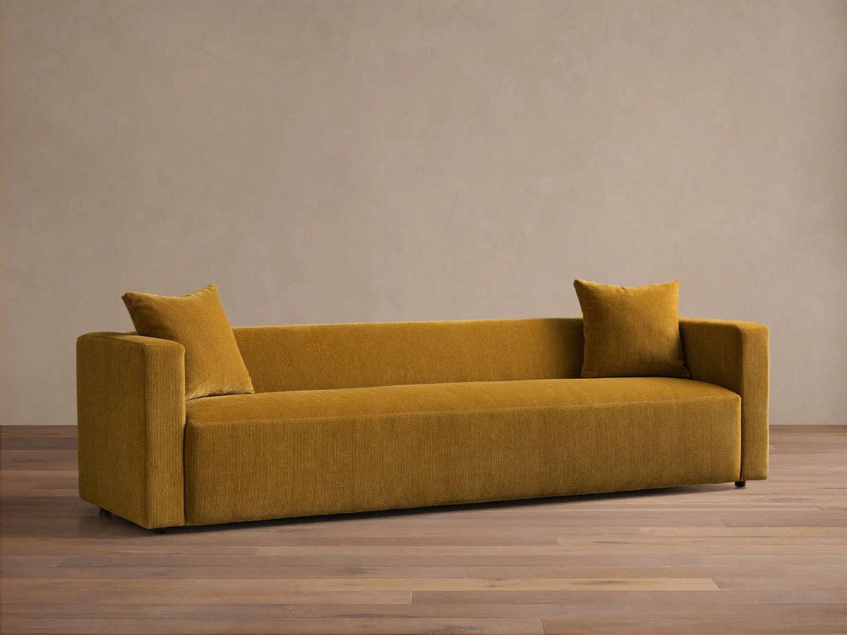 Front view of the mustard yellow Brady Sofa, a modern, rectangular sofa with square arms and two matching throw pillows.