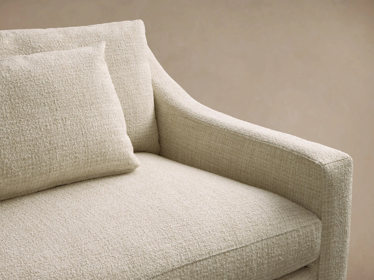 Front view of a light cream Ashby Elevated Sofa with sloped arms, two rectangular accent pillows, and mocha finish wooden legs.