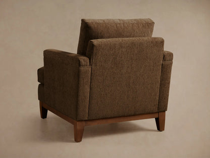 Close-up, angled view of a brown upholstered armchair, featuring a textured fabric on the armrest, seat cushion, and back cushion.
