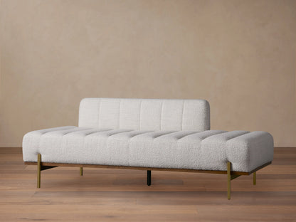 Lansing Daybed in light grey fabric with a tufted, cushioned seat and backrest, gold metal legs, on a wooden floor.