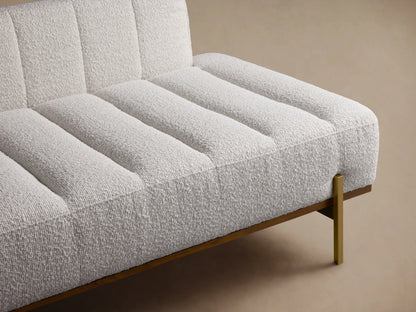 Lansing Daybed with soft beige upholstery, tufted design, and minimalist brass legs on a wooden floor, against a beige wall.