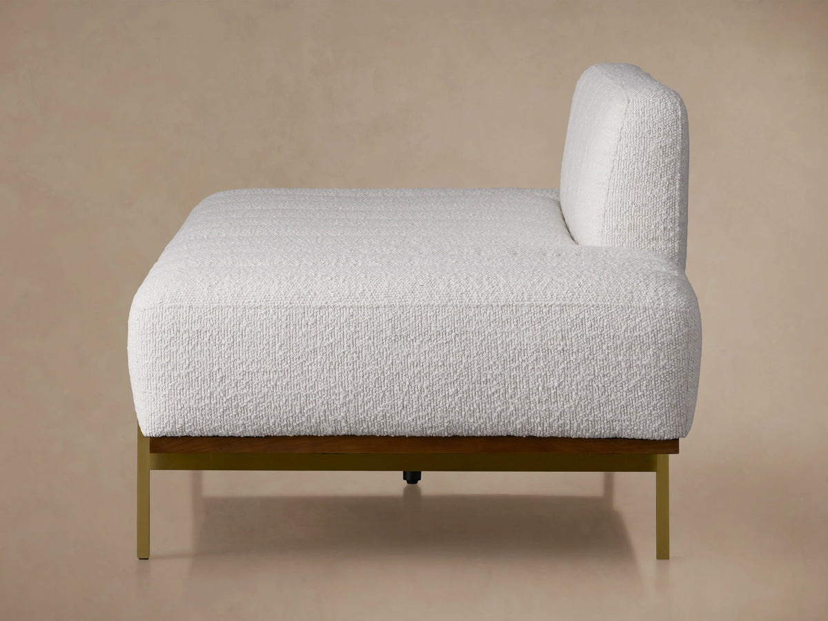 Lansing Daybed featuring a soft gray fabric, wooden base, and metal legs. Backrest central, cushions extend from sides. Beige wall background.