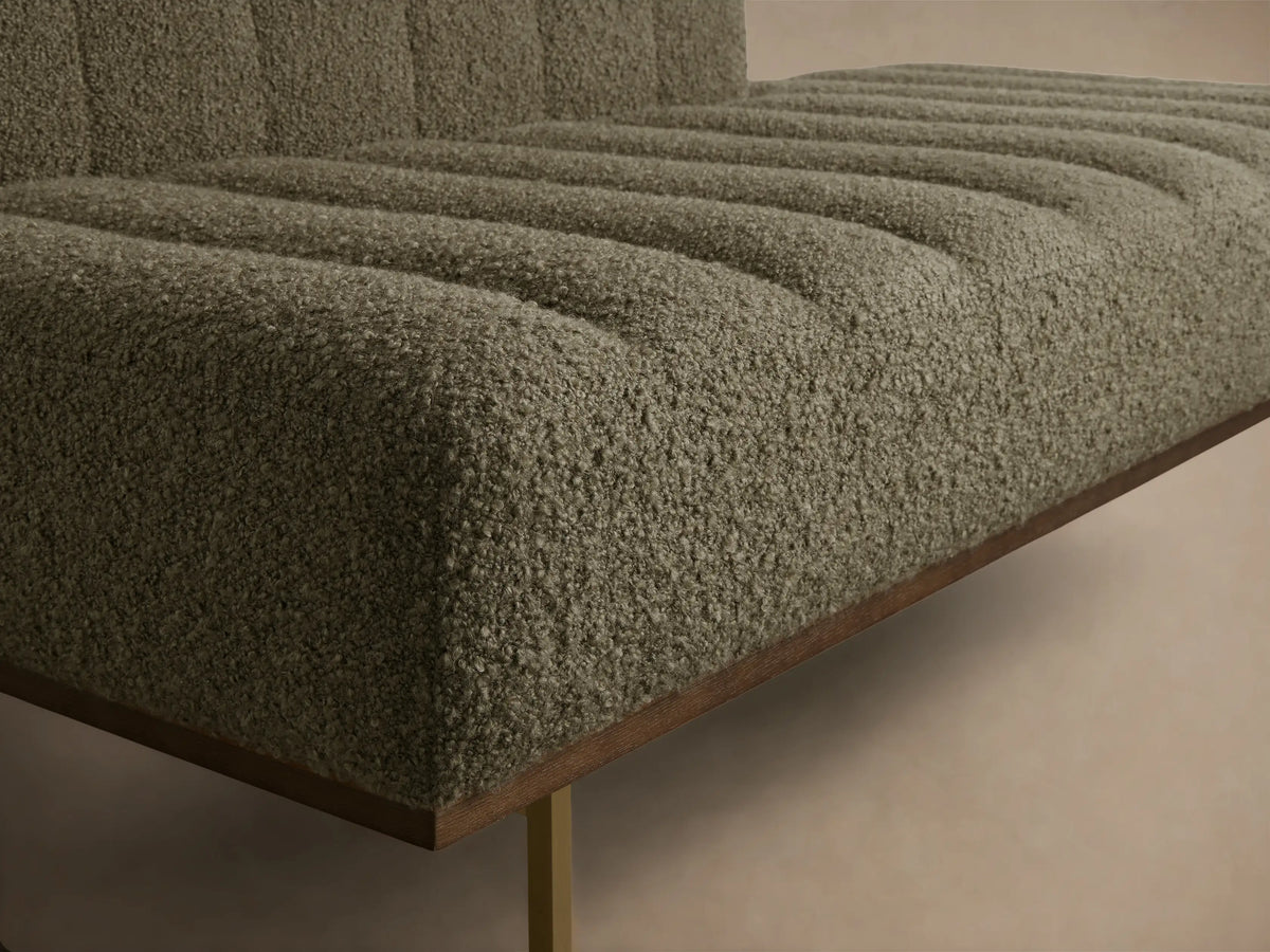 Close-up of a greige bouclv© bench, featuring ribbed upholstery on the seat and back, with a dark wood base and gold leg.