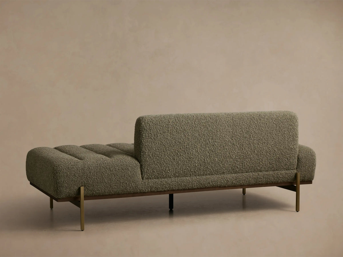 Angled view of an olive green bouclv© chaise lounge with channeled seat, dark wood frame, and brass legs.
