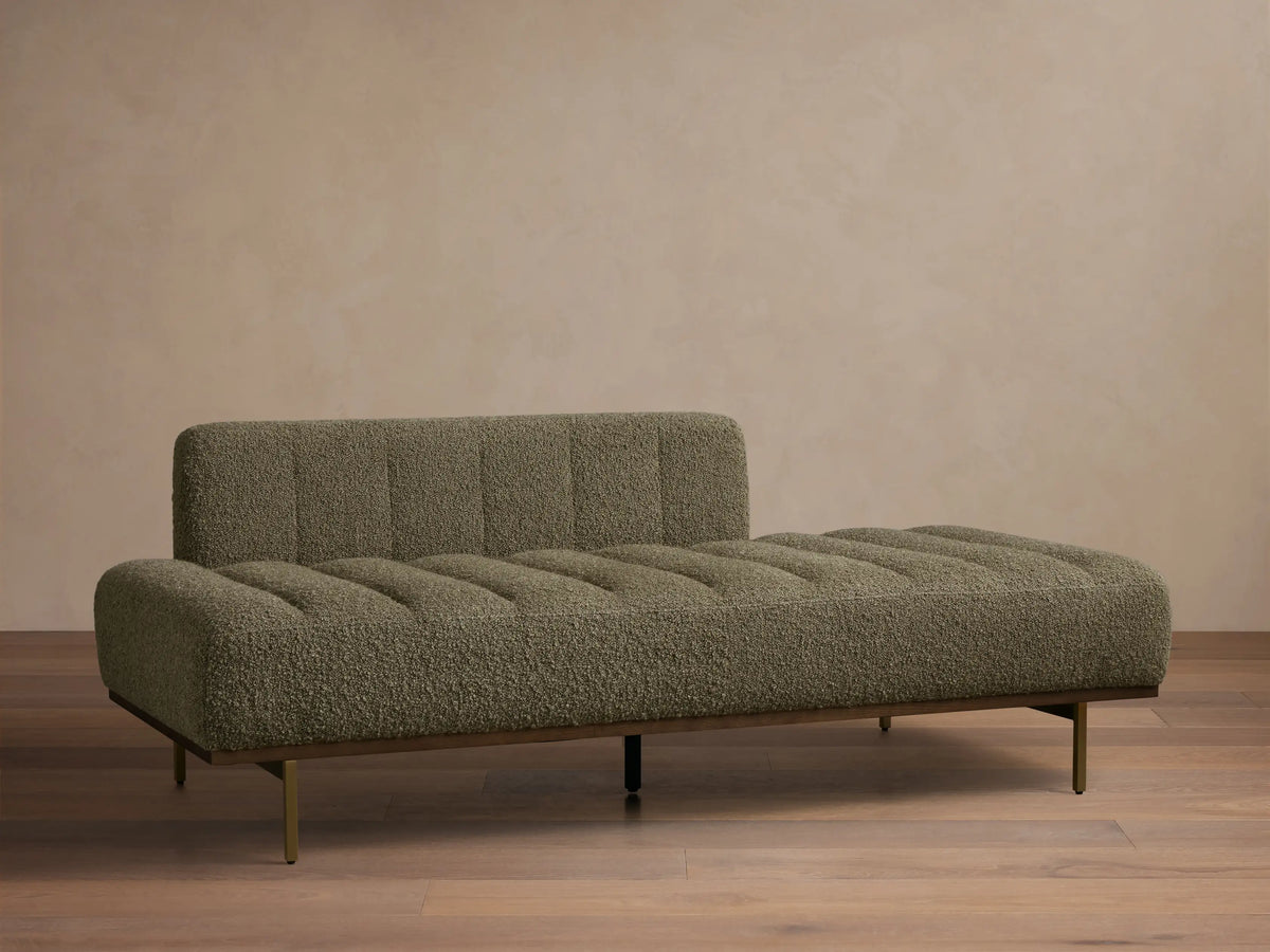 Front view of an olive green boucle chaise lounge with horizontal channel tufting, a dark wood frame, and slender brass legs.