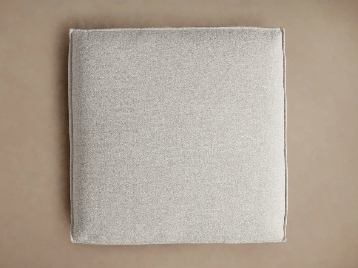Overhead view of the light gray Coburn Ottoman, a soft square cushion with fine texture and piping along the seams.