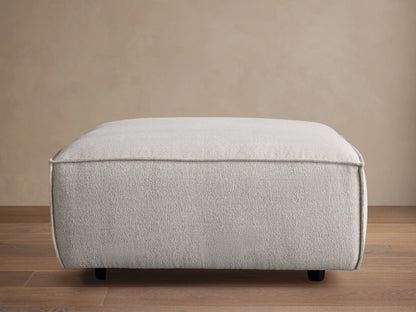 Top view of a light grey textured Coburn Ottoman with visible piping along the edges.