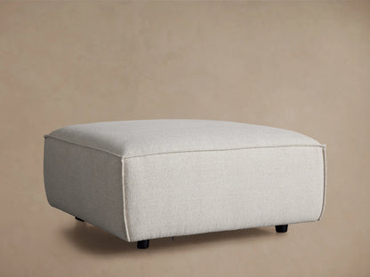 Front view of a light beige Coburn Ottoman with visible piping details.