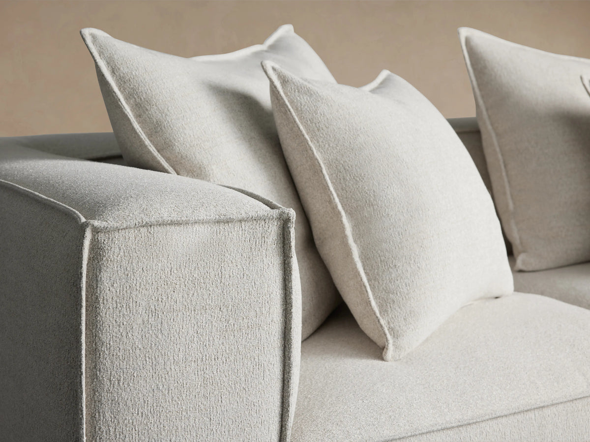 Coburn Four-Piece Sectional in light beige fabric, featuring large plush back cushions and a sleek, modern rectangular design, on wooden floor.