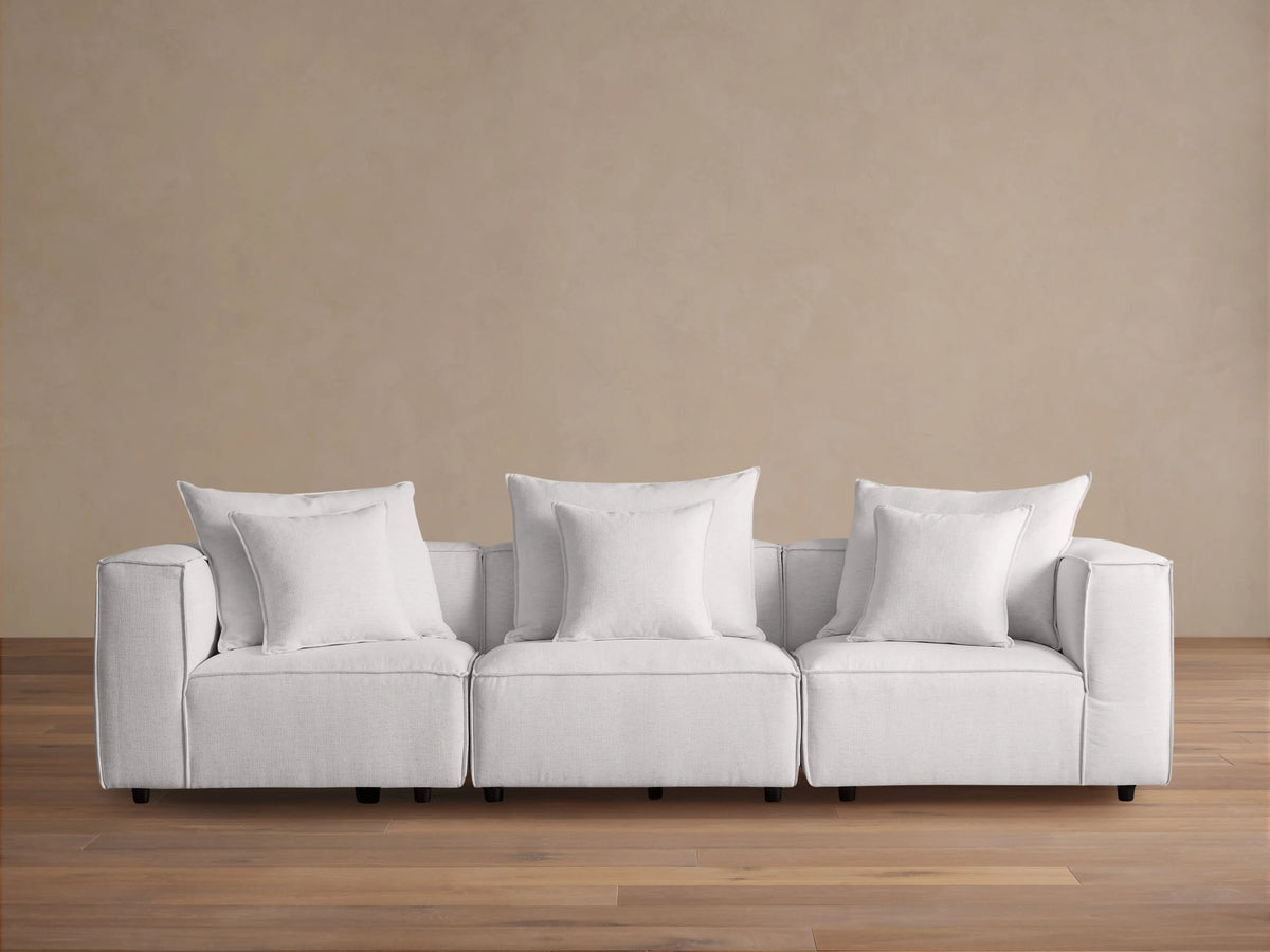 Coburn Three Piece Modular Sofa in light gray fabric, featuring three sections with plush cushions and pillows in a minimalist setting.