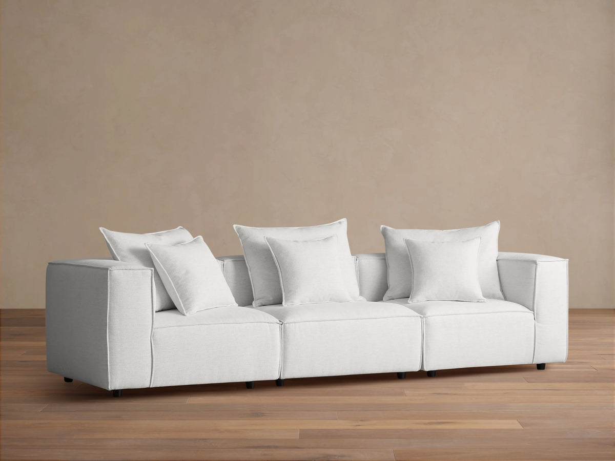 Coburn Three Piece Modular Sofa in light gray fabric, featuring three sections with plush cushions and pillows in a minimalist setting.