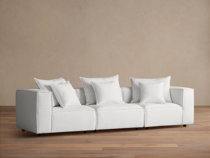 Coburn Three Piece Modular Sofa in light gray fabric, featuring three sections with plush cushions and pillows in a minimalist setting.