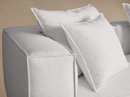 White Coburn Three Piece Modular Sofa with three sections, plush cushions, and padded armrests on a wooden floor against a neutral wall.