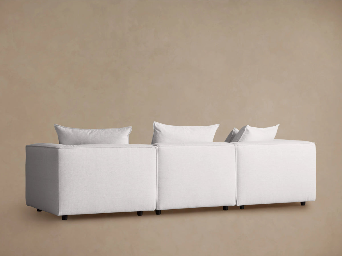 Coburn Three Piece Modular Sofa in light fabric, features plush back pillows and sleek, angular armrests for a modern look.