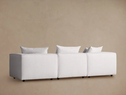Coburn Three Piece Modular Sofa in light fabric, features plush back pillows and sleek, angular armrests for a modern look.