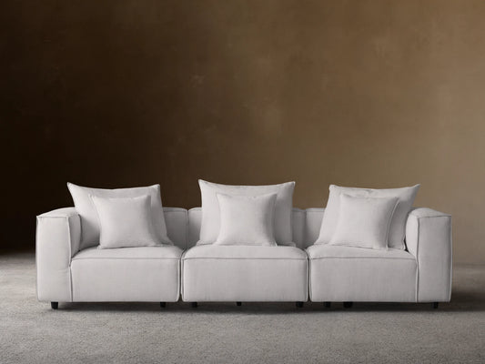 Coburn Three Piece Modular Sofa in light gray fabric, featuring three sections with plush cushions and pillows in a minimalist setting.