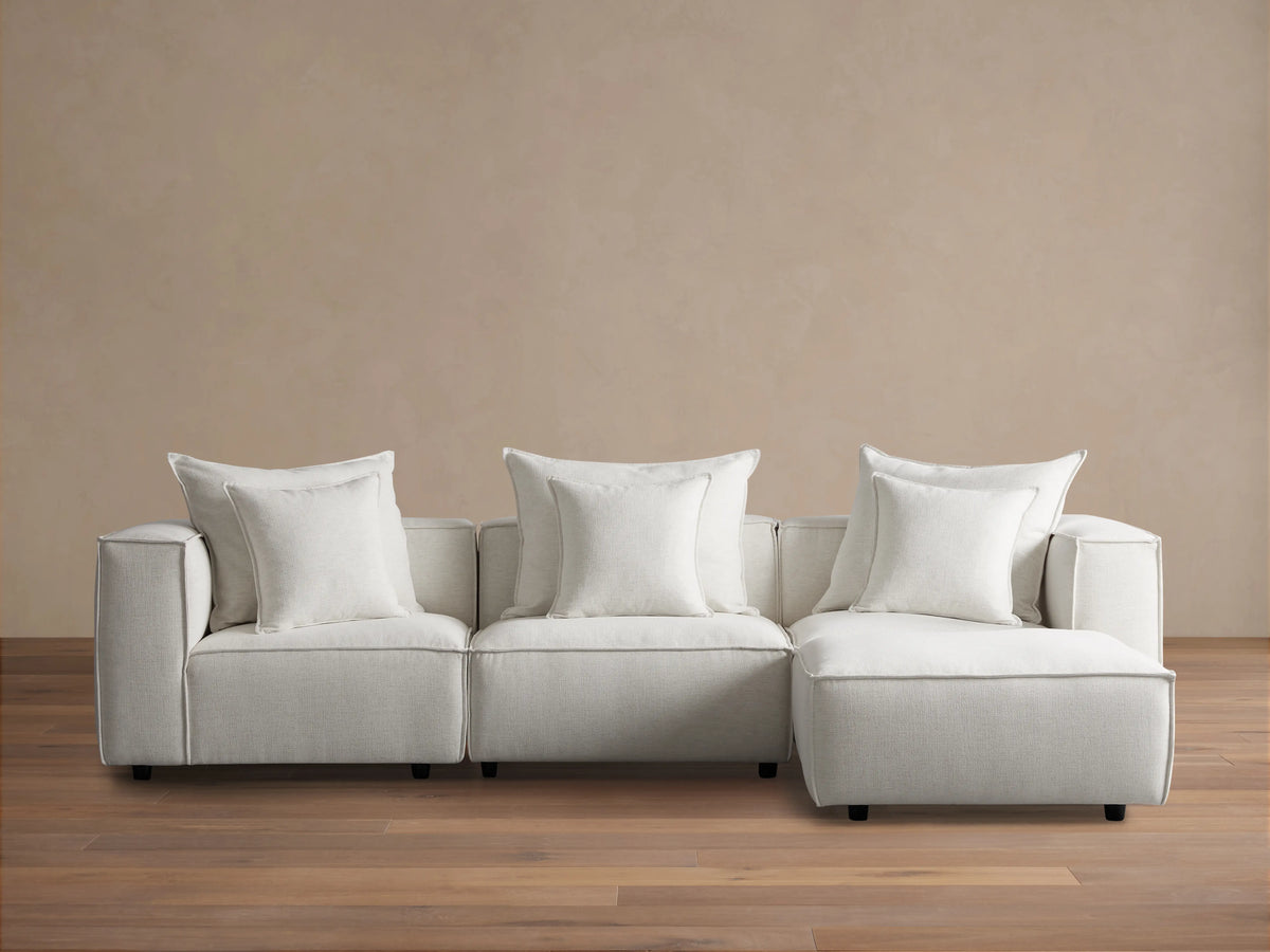 Coburn Four-Piece Sectional in light beige fabric, featuring three seats and a chaise, set against a light brown wall on wood flooring.