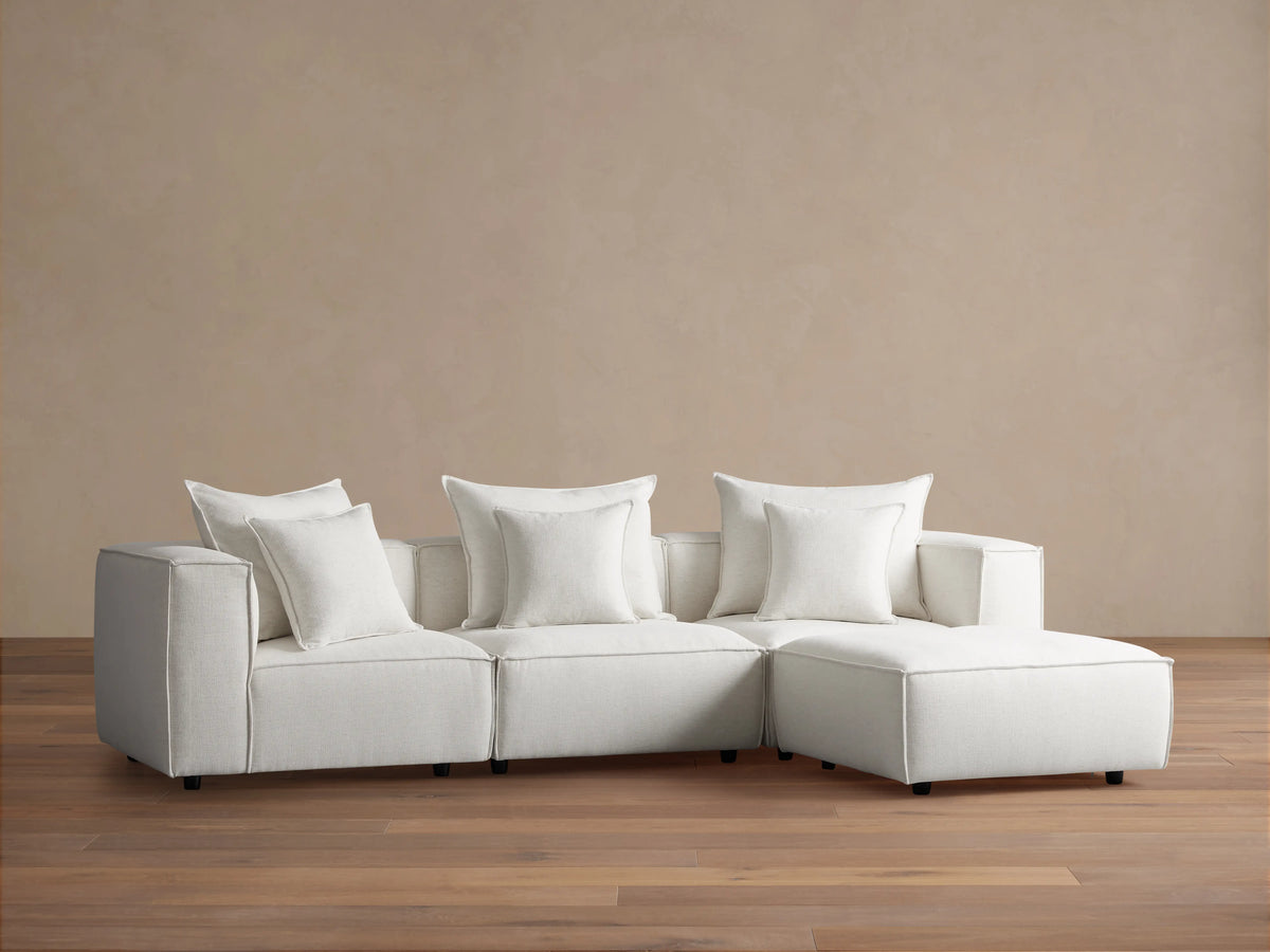Coburn Four-Piece Sectional in light beige fabric, featuring three seats and a chaise, set against a light brown wall on wood flooring.
