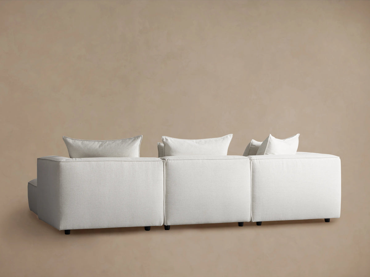 Coburn Four-Piece Sectional in light fabric, featuring solid blocks with plush cushions, on wooden floor against beige wall.
