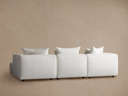 Coburn Four-Piece Sectional in light fabric, featuring solid blocks with plush cushions, on wooden floor against beige wall.