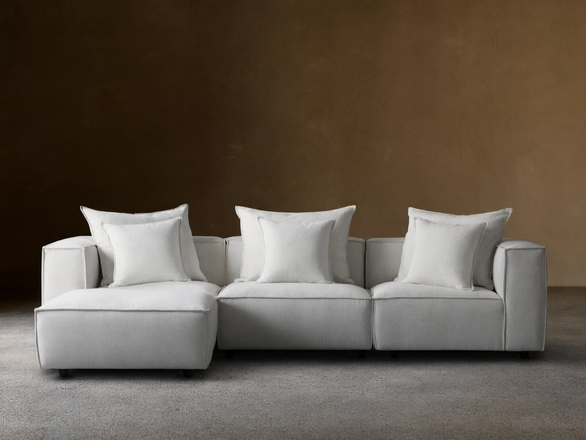 Coburn Four-Piece Sectional in light beige fabric, featuring three seats and a chaise, set against a light brown wall on wood flooring.