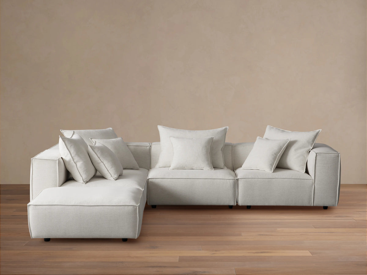 Coburn Five-Piece Sectional, L-shaped, upholstered in light grey fabric, with many soft accent pillows, on a wood floor.