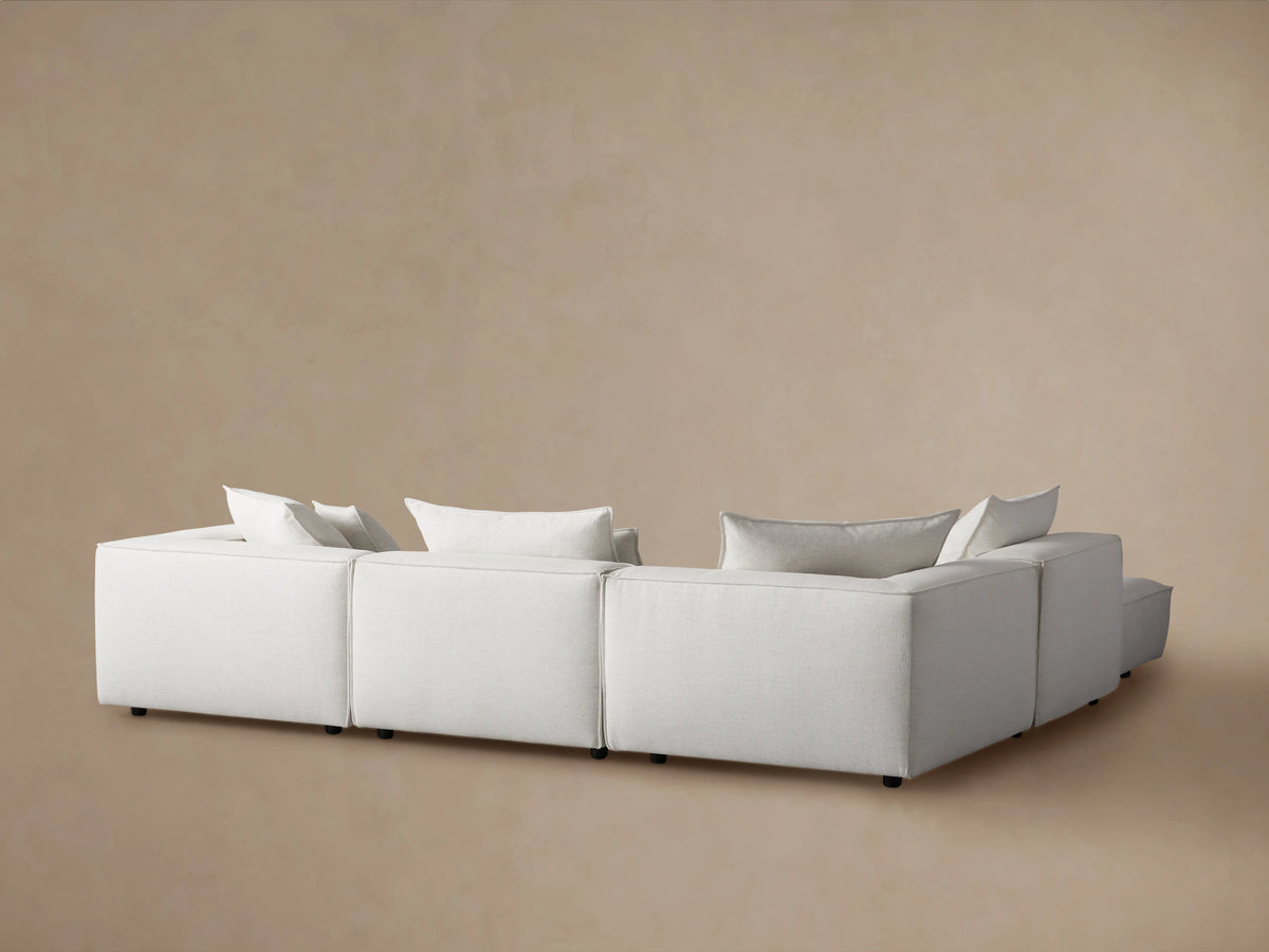 Coburn Five-Piece Sectional, off-white modular sofa with plush back pillows, angled view from behind against a beige wall.